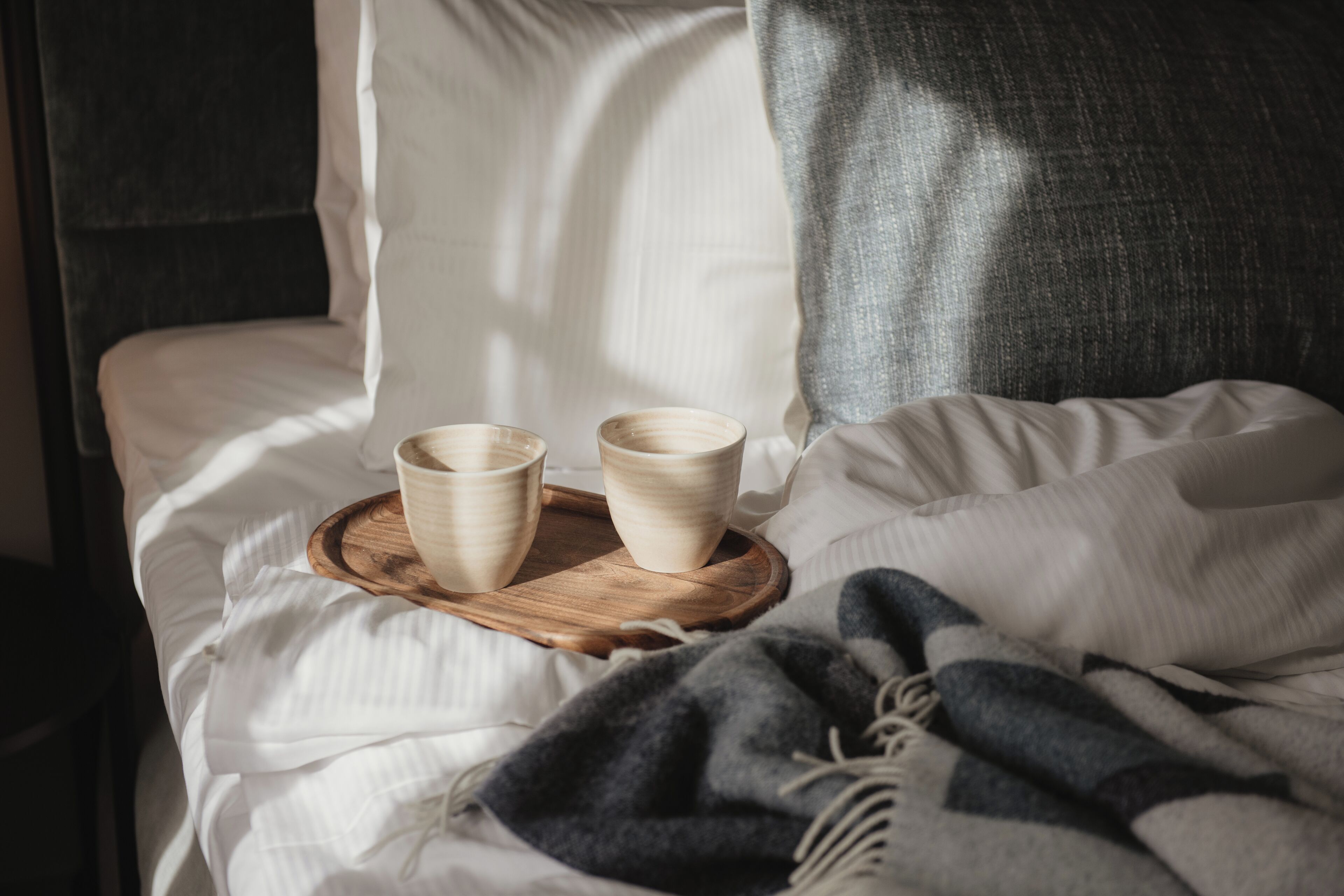 A bed with white linens, a wooden tray with two bowls, and a gray blanket.