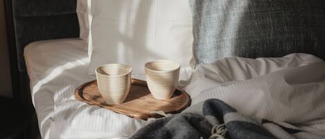 A bed with white linens, a wooden tray with two bowls, and a gray blanket.