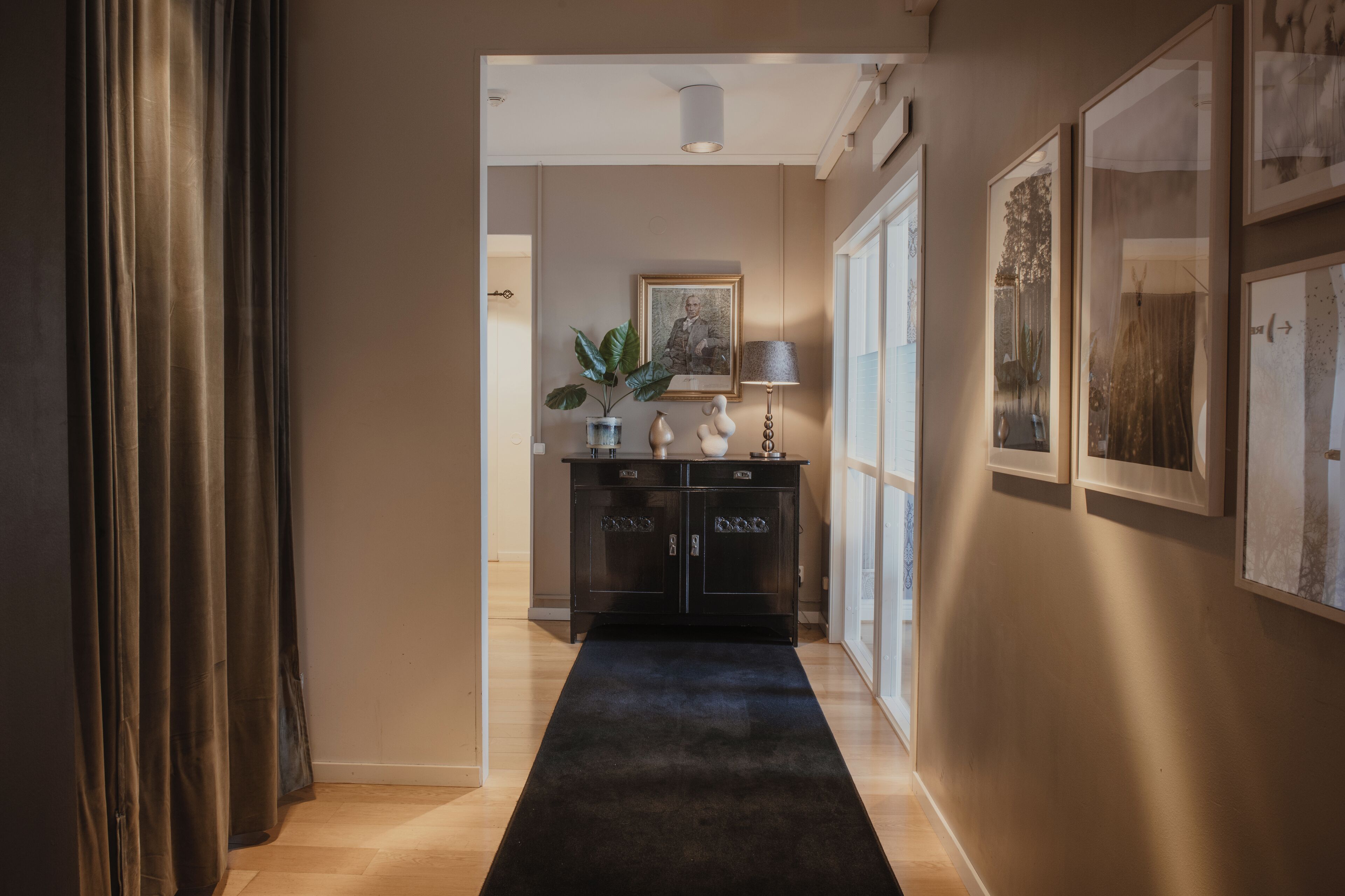 Un pasillo con alfombra oscura, un mueble negro con adornos y cuadros en las paredes.