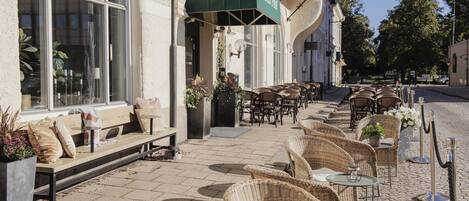 A hotel exterior with outdoor seating, a green awning, and a cobblestone patio.