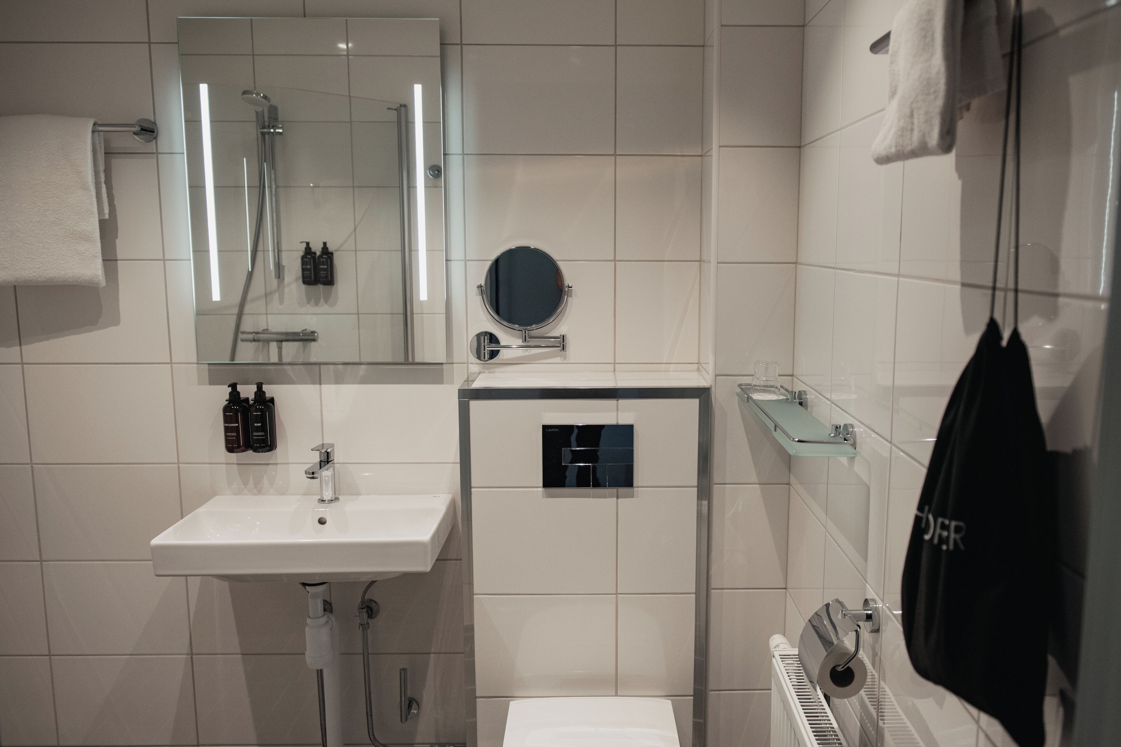 A modern bathroom with a white sink, a mirror, a shower, and a towel rack.