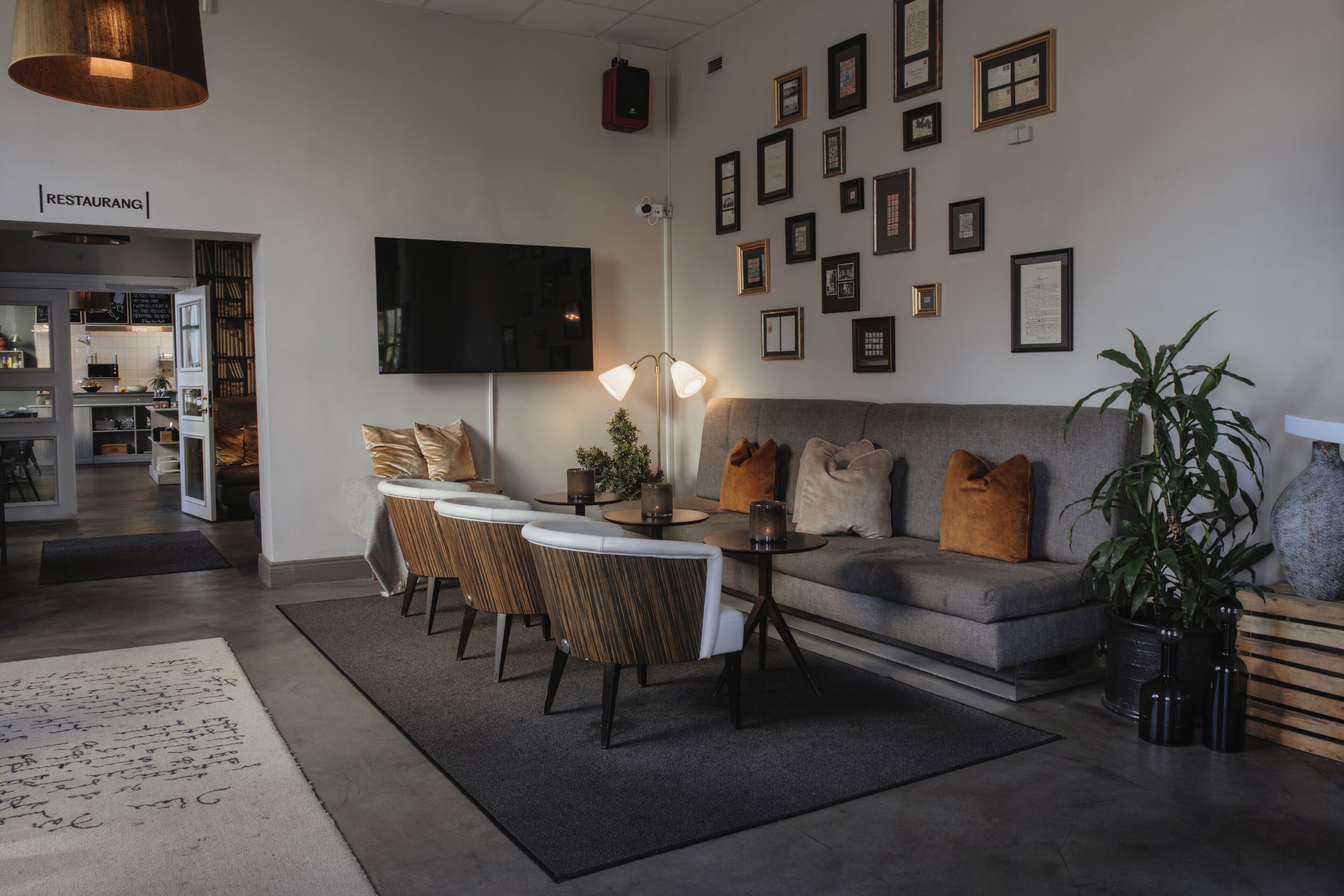Una sala de estar moderna con un sofá gris, una mesa de comedor con sillas, un televisor de pantalla plana montado en la pared y varias fotografías enmarcadas.