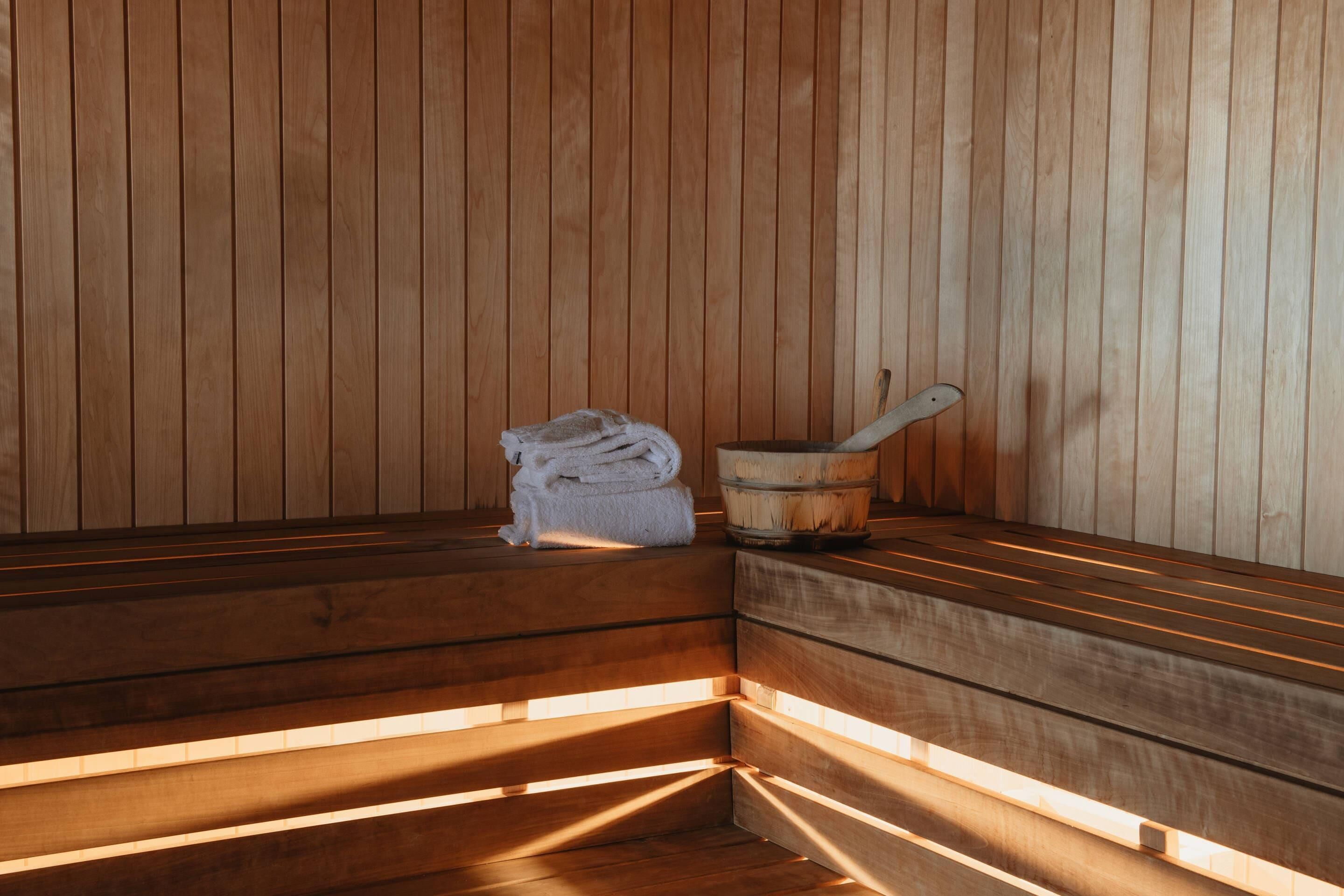 Una sauna con bancos de madera y un cubo de madera con una cuchara.