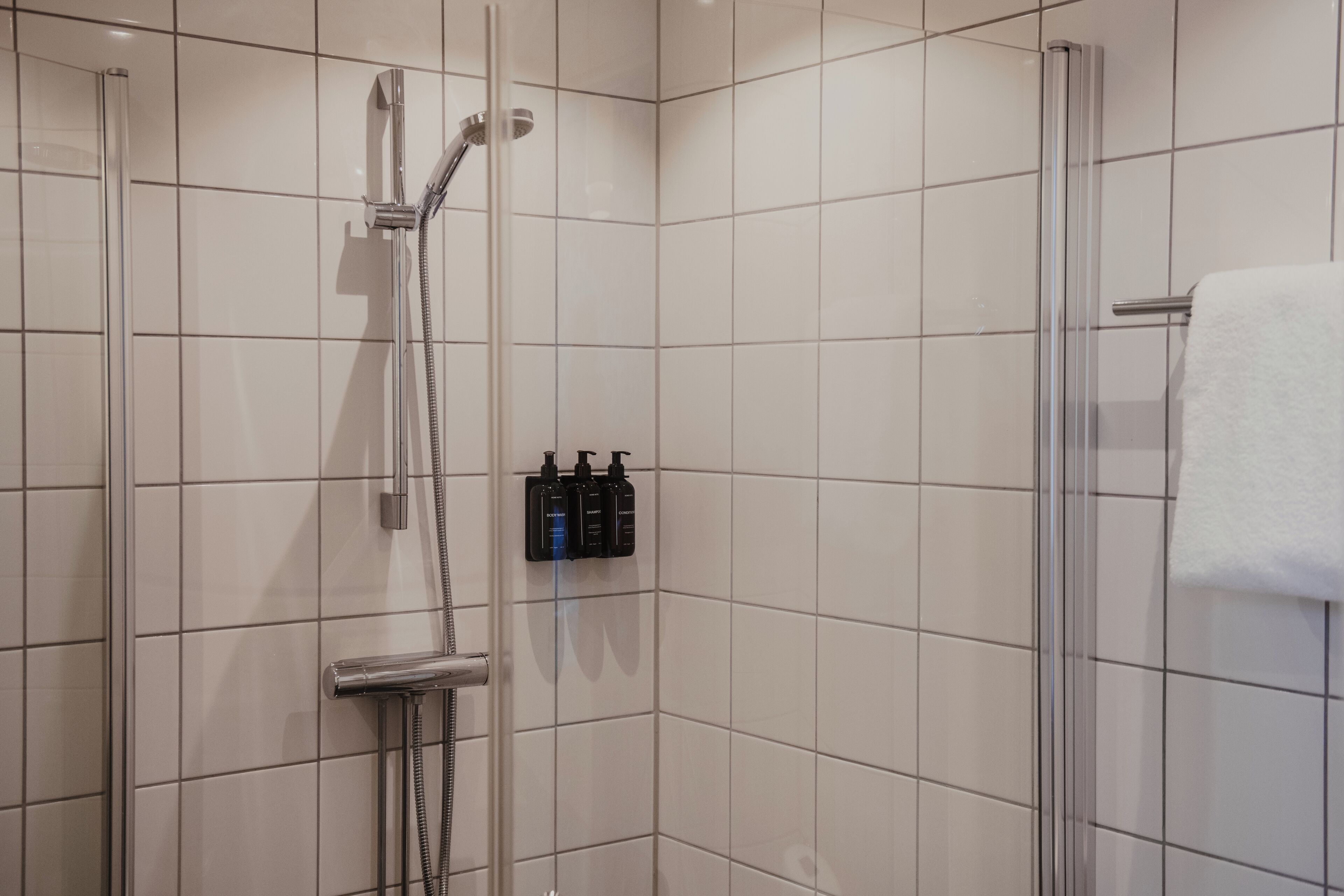 Ein Duschbereich mit Glastür, Handbrause und einer Reihe von Pflegeprodukten an der Wand.