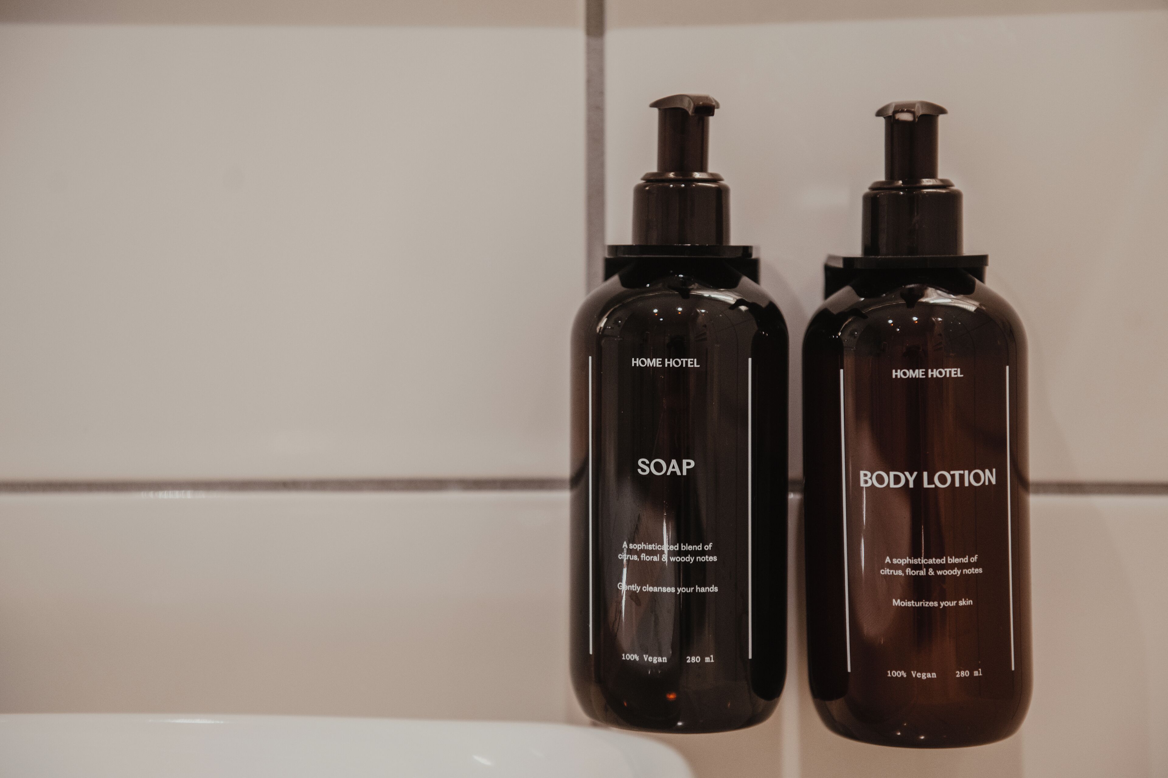 Two bottles of soap and body lotion on a tiled wall.
