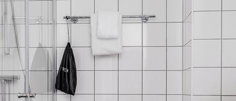 A modern bathroom with a white toilet, a glass shower enclosure, a black trash bin, and a towel rack with a white towel.