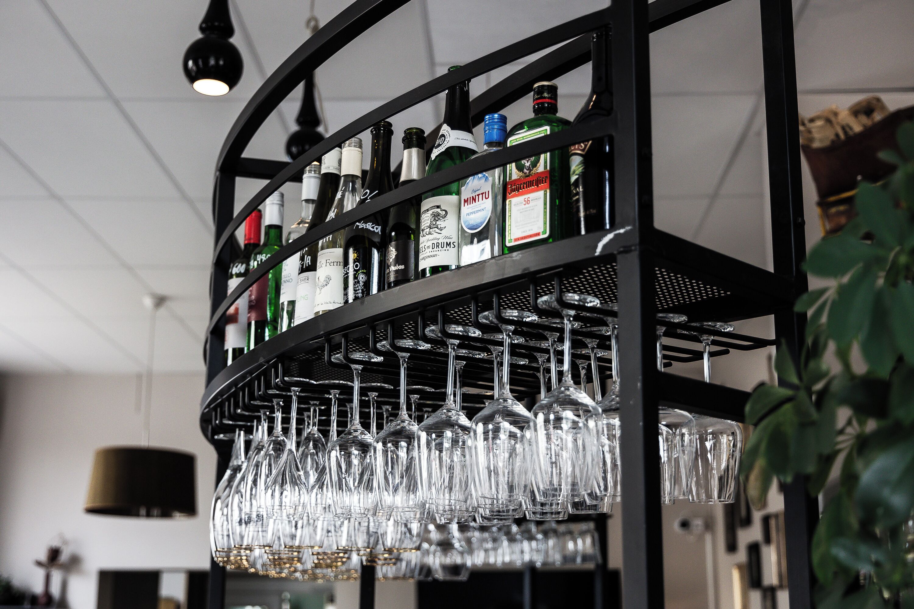 Zona de bar con estantes llenos de botellas de licores y copas de vino colgantes.