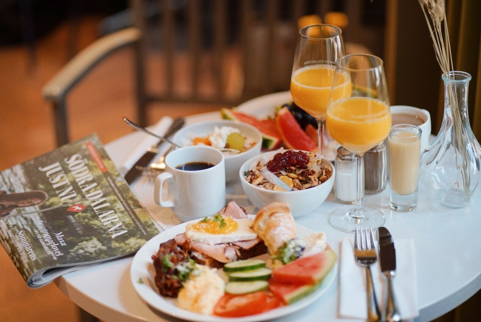 A breakfast table with a variety of food items, including toast, eggs, and fruit, along with beverages and a magazine.