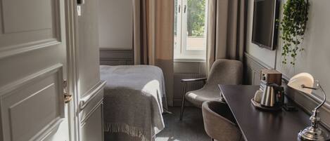 A hotel room with a bed, a desk with a lamp, a chair, a television, and a window with curtains.