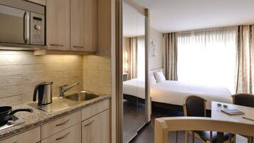 A modern hotel room with a kitchenette, a bed, a dining area, and a view of the outdoors.