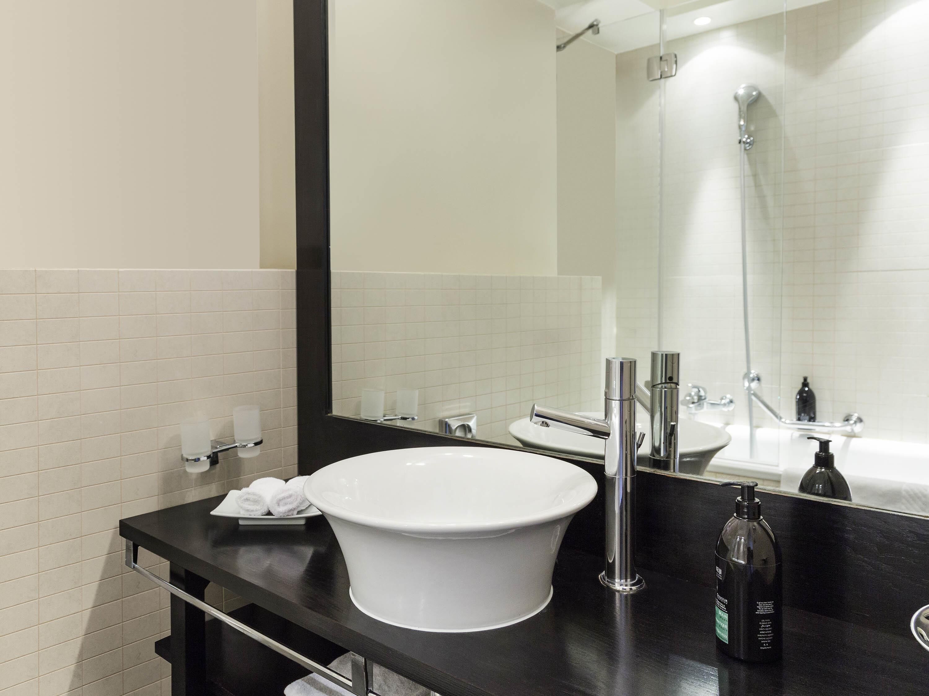 Een moderne badkamer met een witte wastafel, een grote spiegel en een douche.
