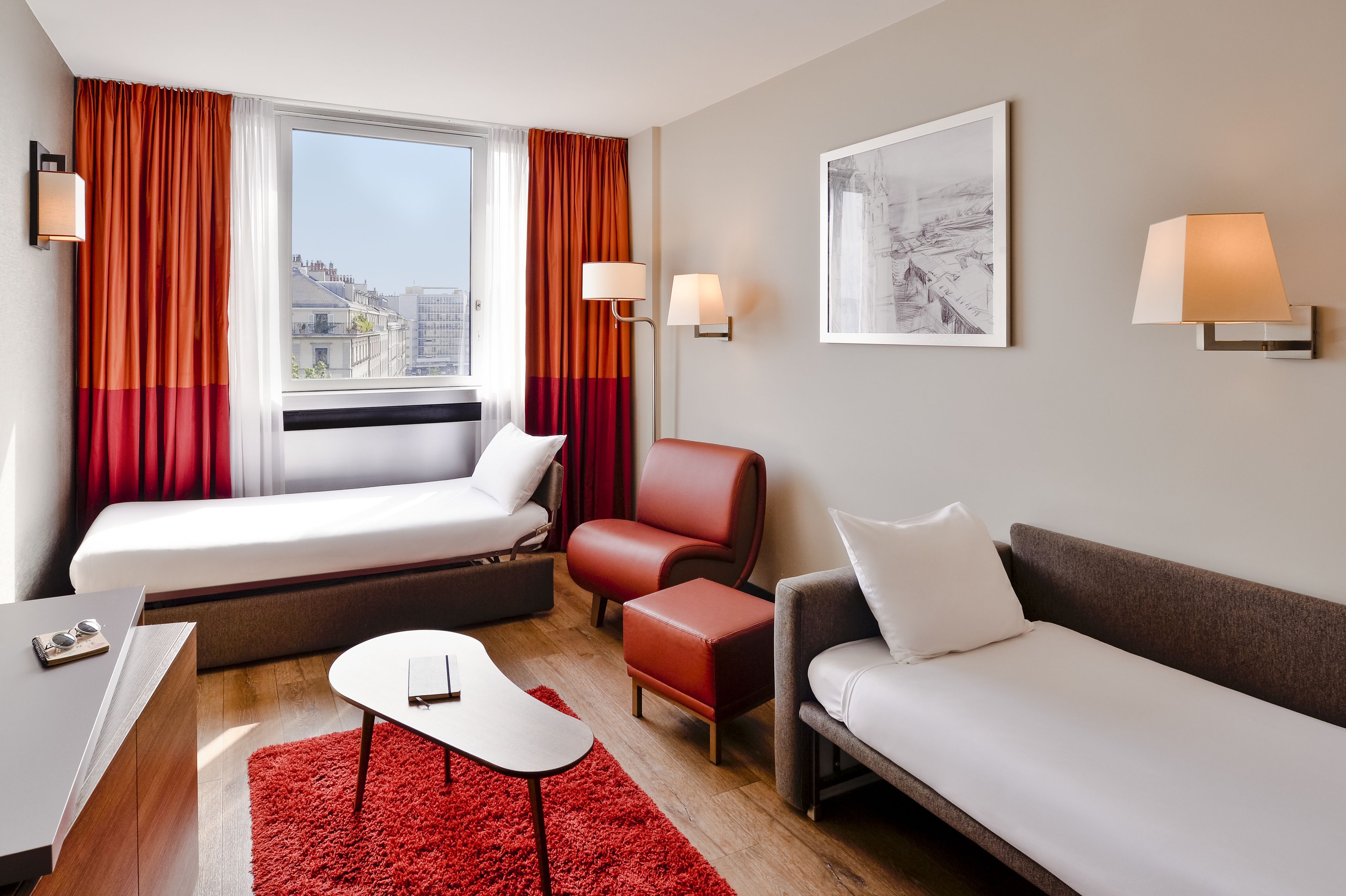 A modern hotel room with a bed, two sofas, a small table, and a red rug.