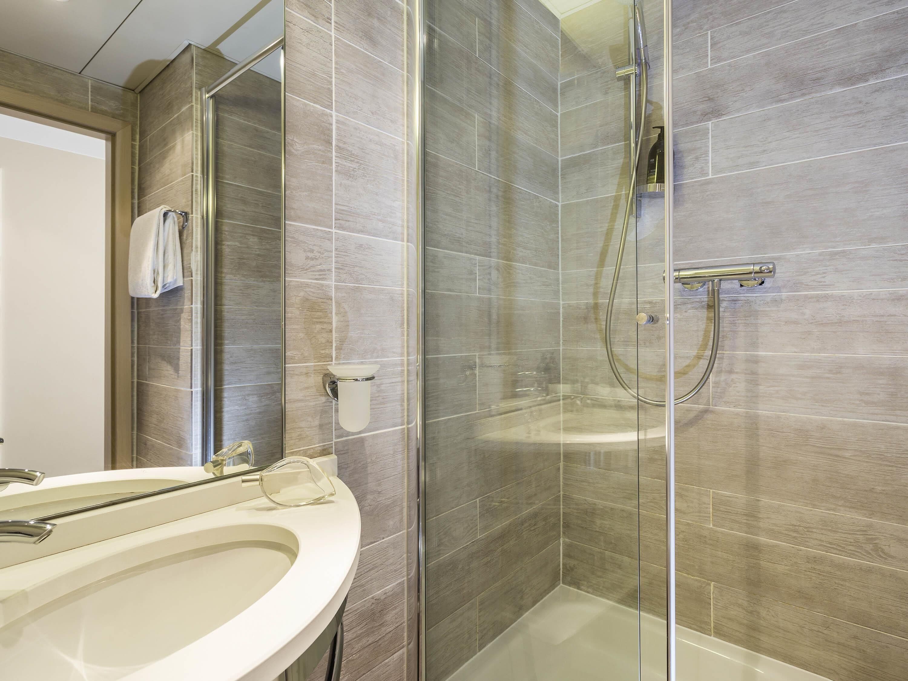 A modern bathroom with a glass-enclosed shower, a white sink, and a towel rack.