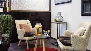 Un salon moderne avec deux fauteuils, une petite table ronde surmontée d’un tapis rouge, un vase décoratif et une plante en pot.