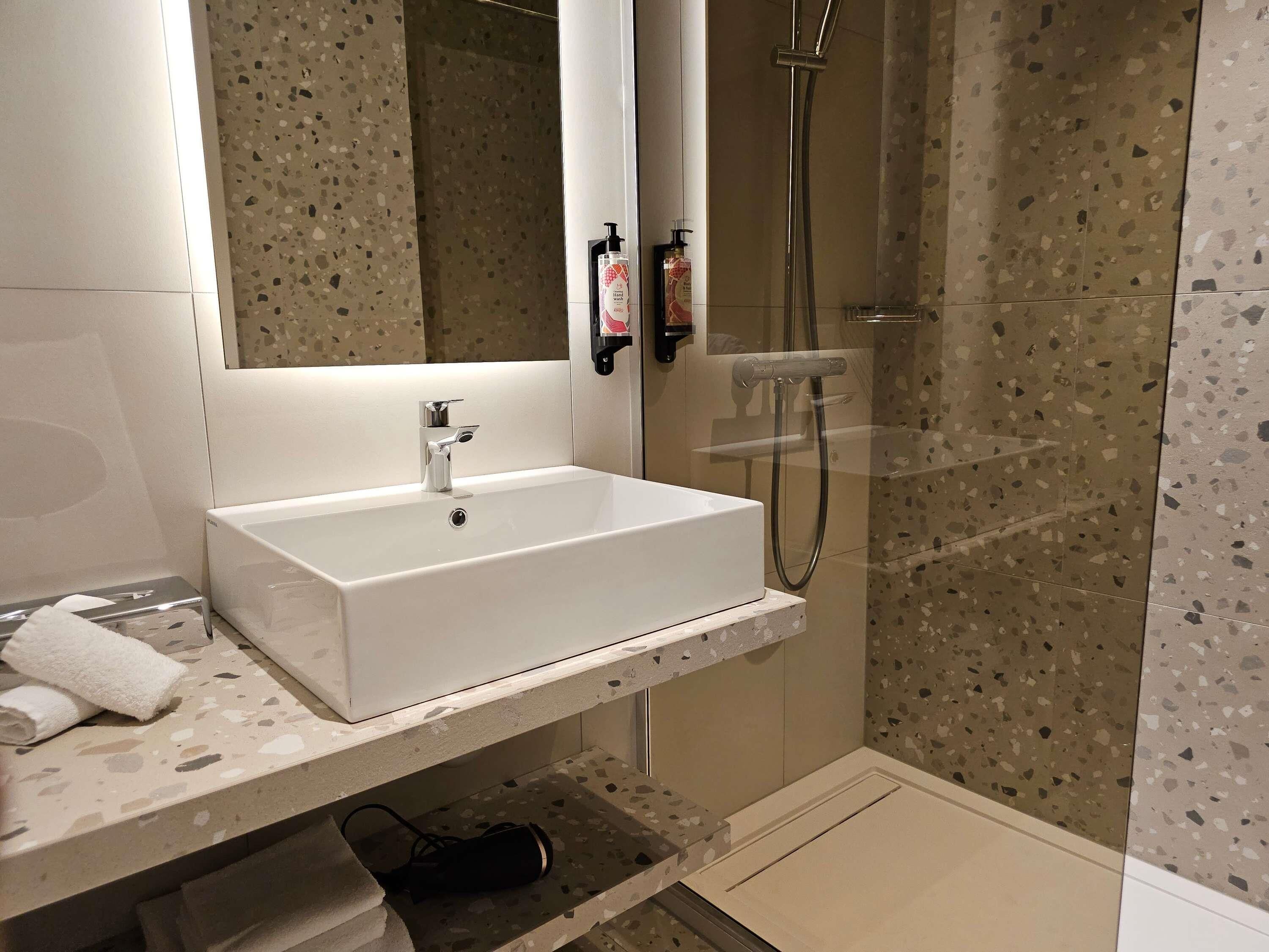 Un baño moderno con lavamanos, espejo y ducha blancos.