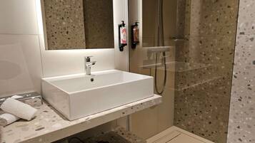 Un baño moderno con lavamanos, espejo y ducha blancos.