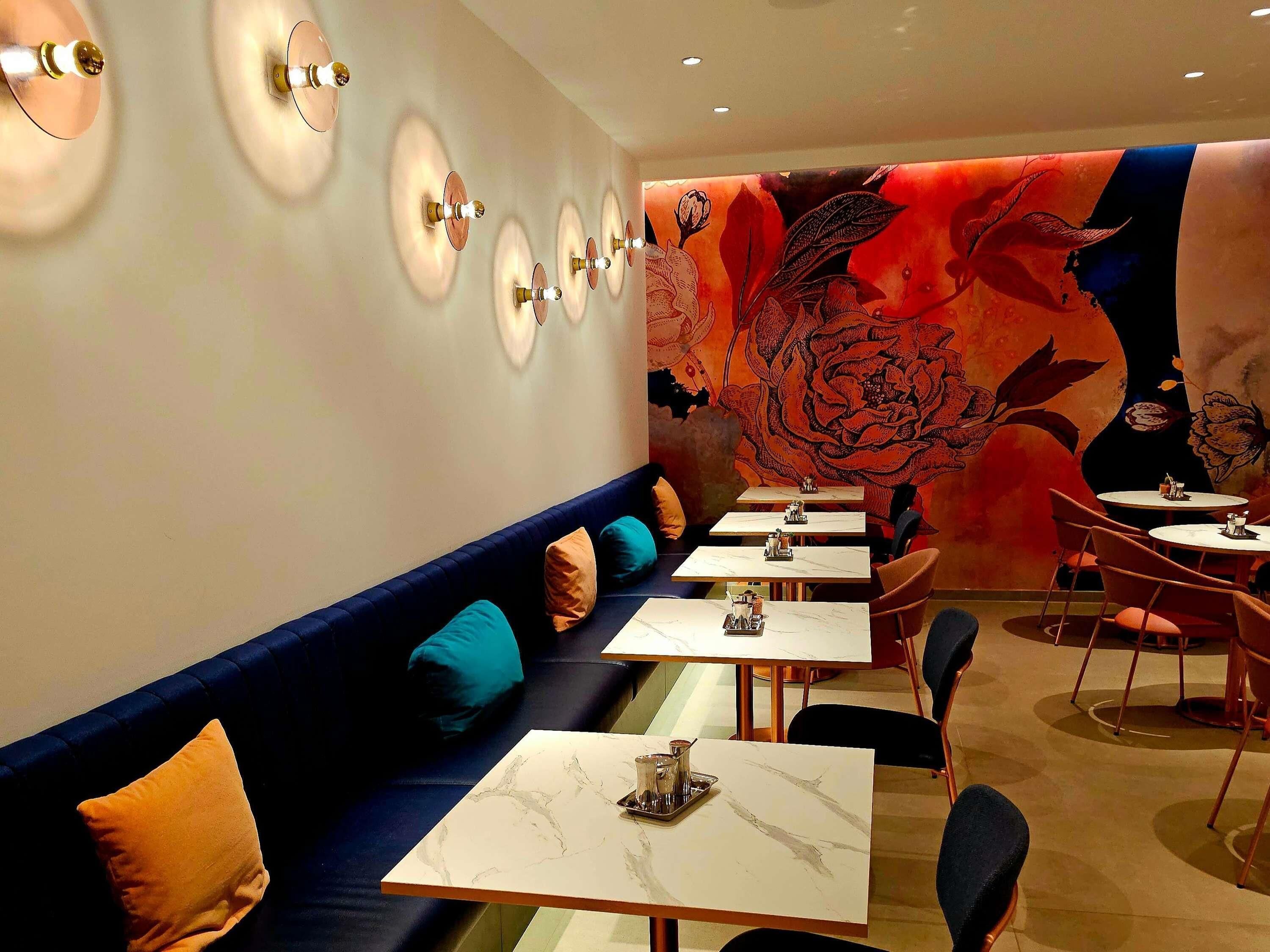 Un ristorante con una lunga area salotto con panche, tavoli e un grande murale floreale sulla parete.