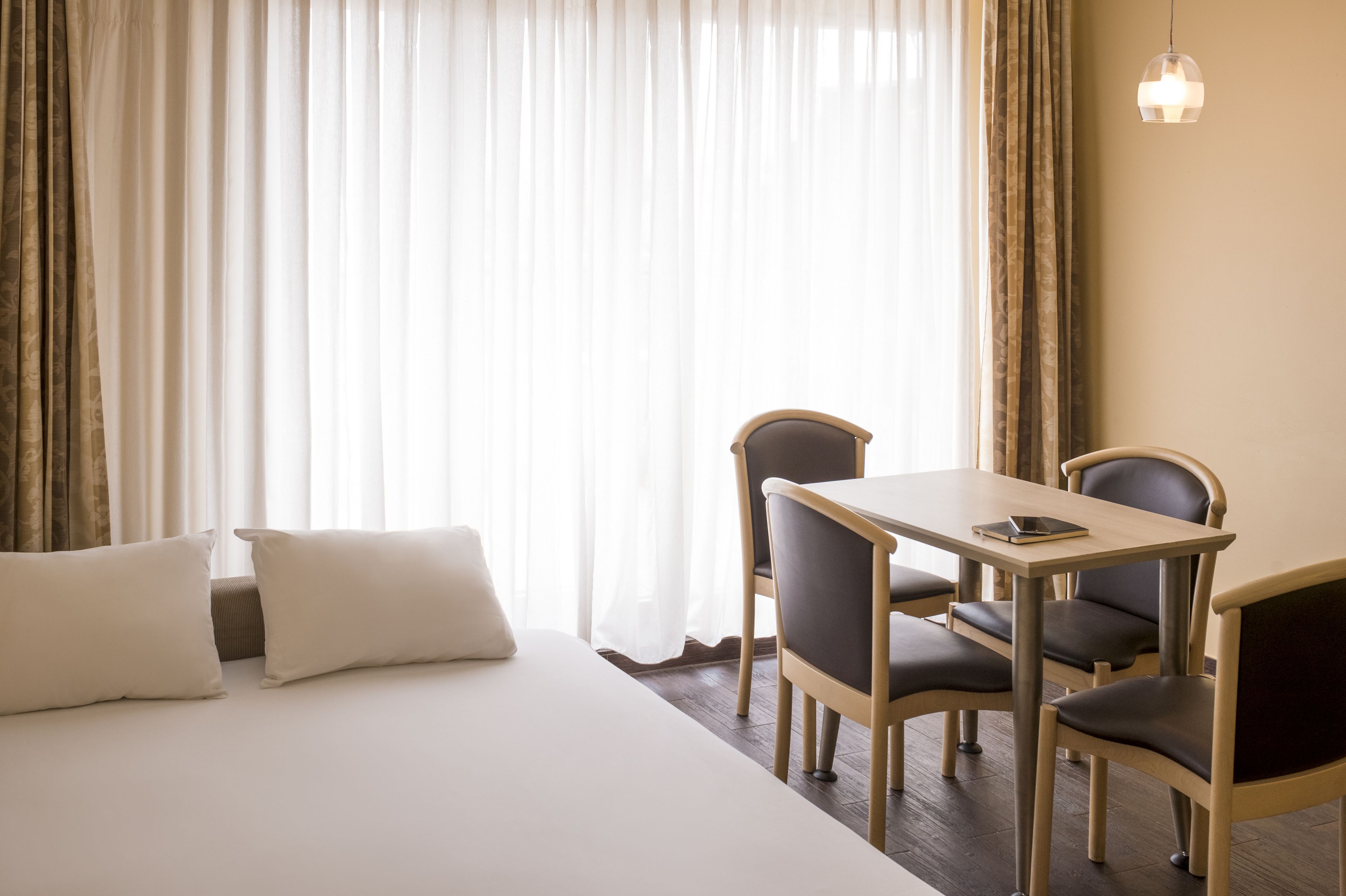 A hotel room with a bed, two chairs, a table, and a hanging light fixture.