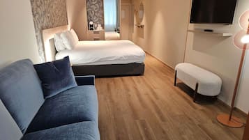 A modern hotel room with a bed, a sofa, a bench, a TV, and a mirror.