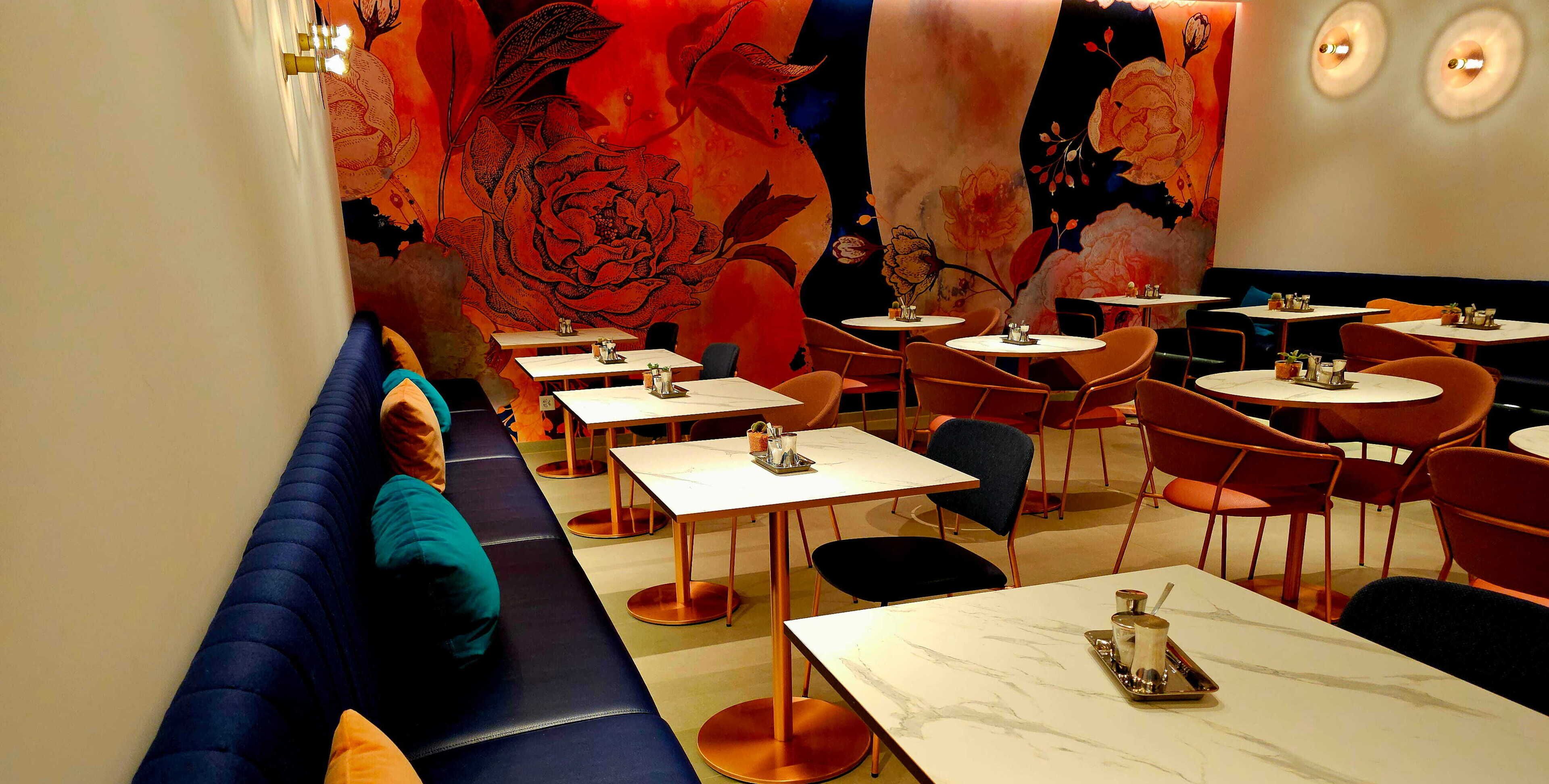 En restaurang med avskilda bås och bord, en väggmålning med blommönster och en modern inredning.