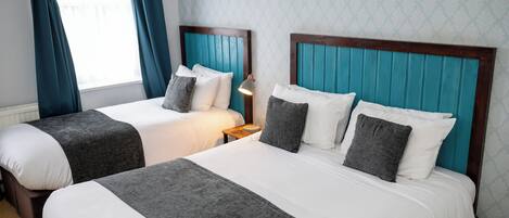 A hotel room with two beds, each with a wooden headboard and grey bedding.