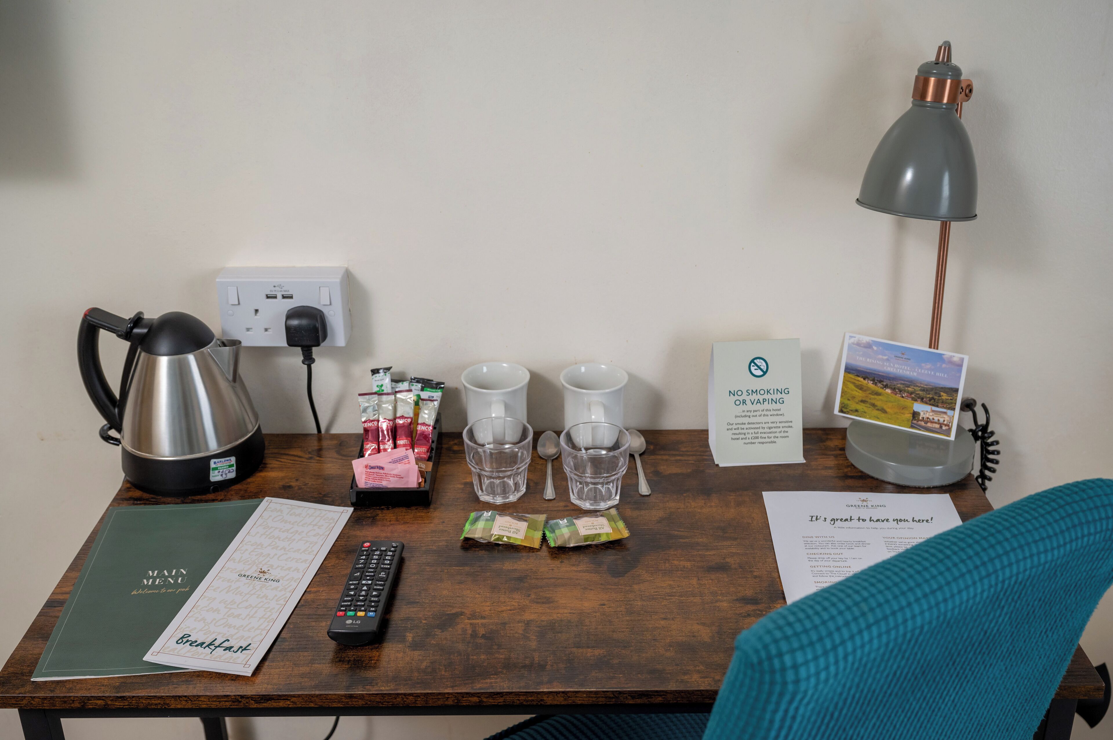 Scrivania in camera d'albergo con bollitore, macchina del caffè, bustine di tè, bicchieri, telecomando e menu.