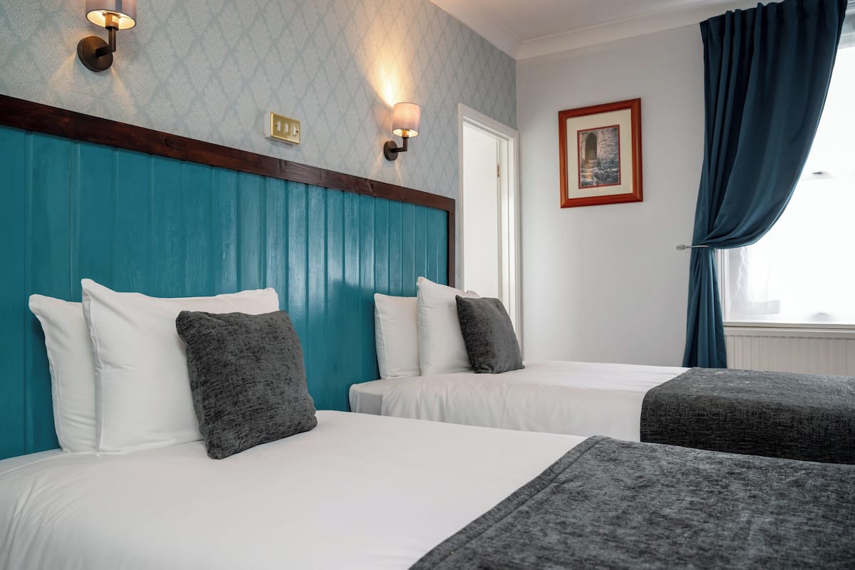 A hotel room with two beds, teal headboard, white bedding, and a framed picture on the wall.