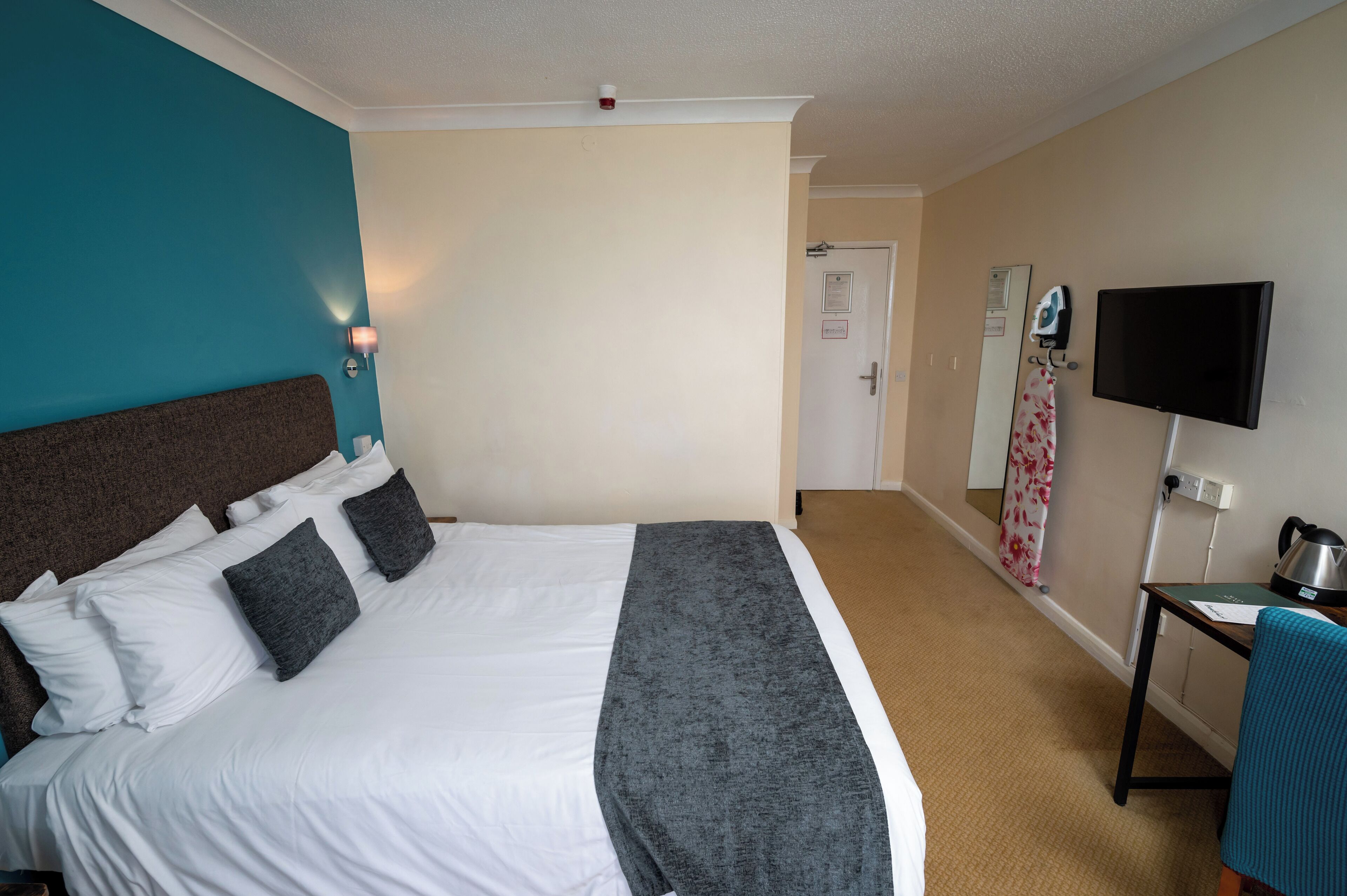 A hotel room with a bed, a desk, a television, and a door.