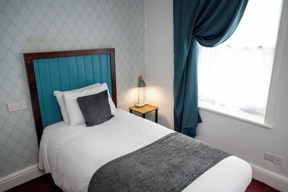 A neatly made bed with a teal headboard, white bedding, and a grey throw blanket.