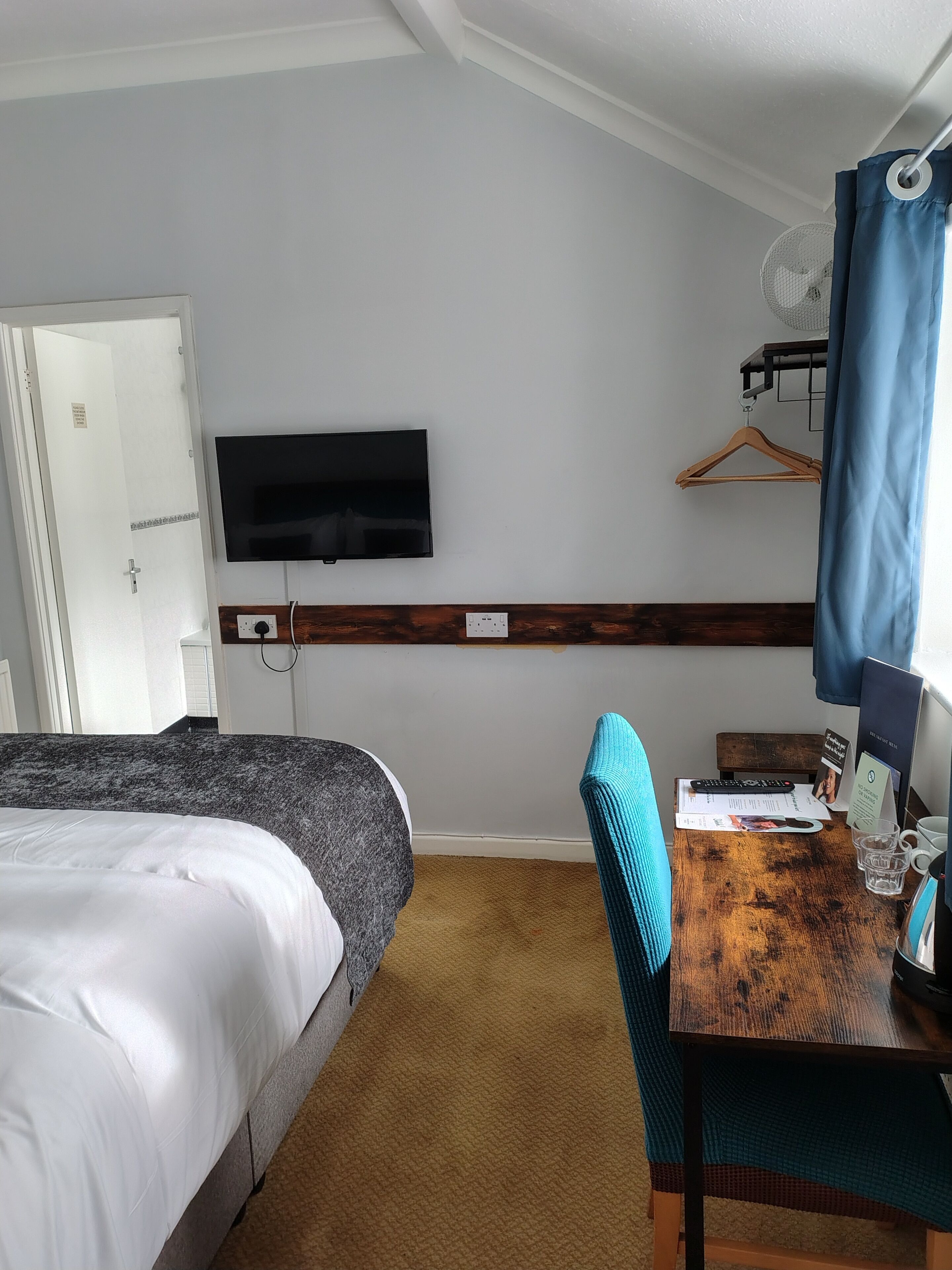 Een hotelkamer met een bed, een bureau met een stoel, een televisie en een raam met gordijn.