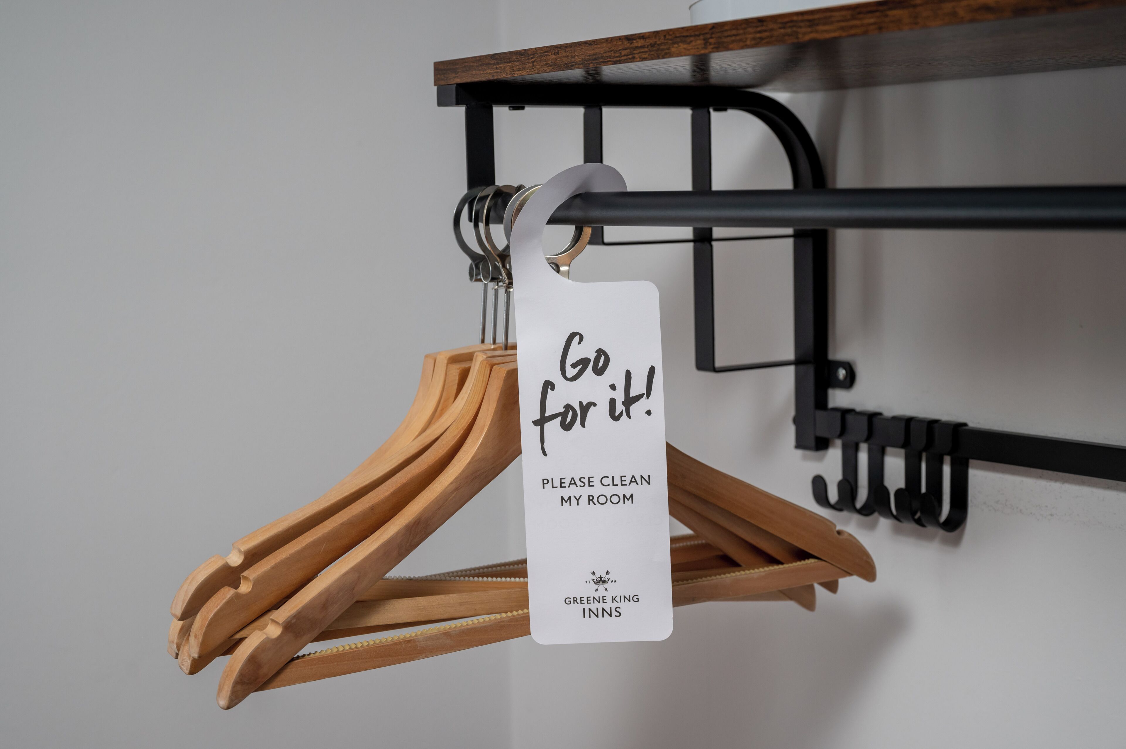 A sign on a coat rack that reads "Go for it! PLEASE CLEAN MY ROOM" with the logo of Greene King Inns.