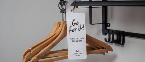 A sign on a coat rack that reads "Go for it! PLEASE CLEAN MY ROOM" with the logo of Greene King Inns.