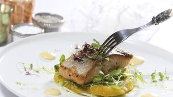 A white plate with a piece of grilled fish, garnished with microgreens and a sauce.