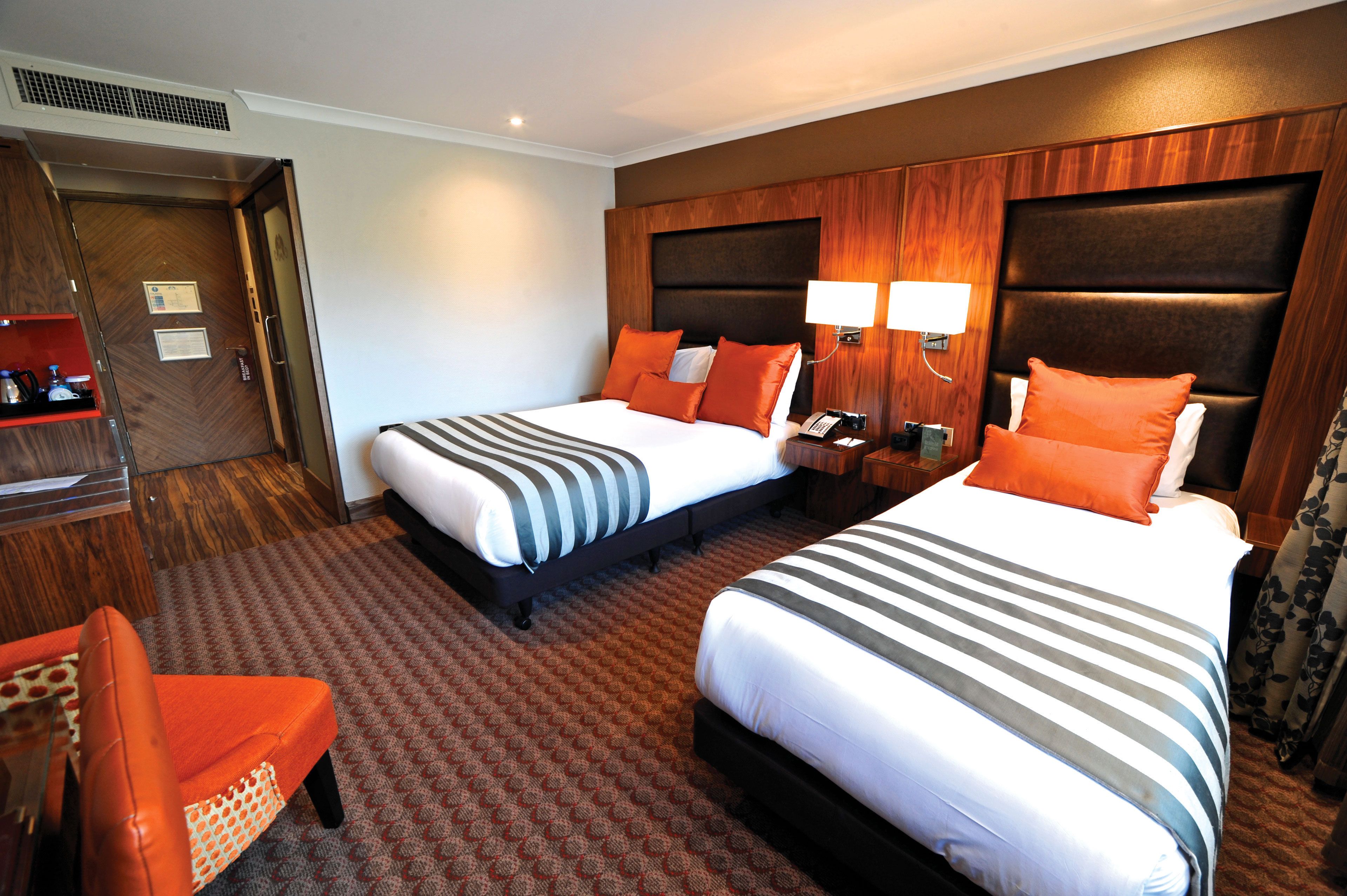 A hotel room with two beds, a wooden headboard, a small desk, and a chair.