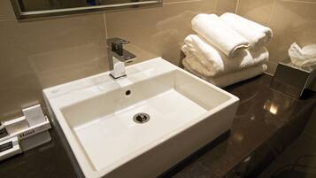 A hotel bathroom with a white sink, a mirror, and a stack of white towels.