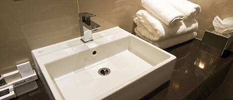 Un baño de hotel con un lavabo blanco, un espejo y una pila de toallas blancas.