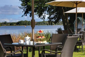 An outdoor dining area with wicker chairs and a table set for a meal, overlooking a lake. - Frensham Pond Country House Hotel & Spa (Farnham)