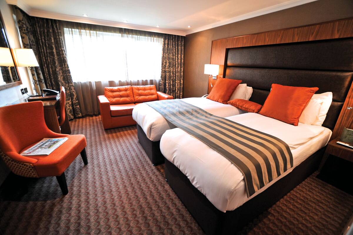 A hotel room with a large bed, two armchairs, a desk, and a large window with curtains.