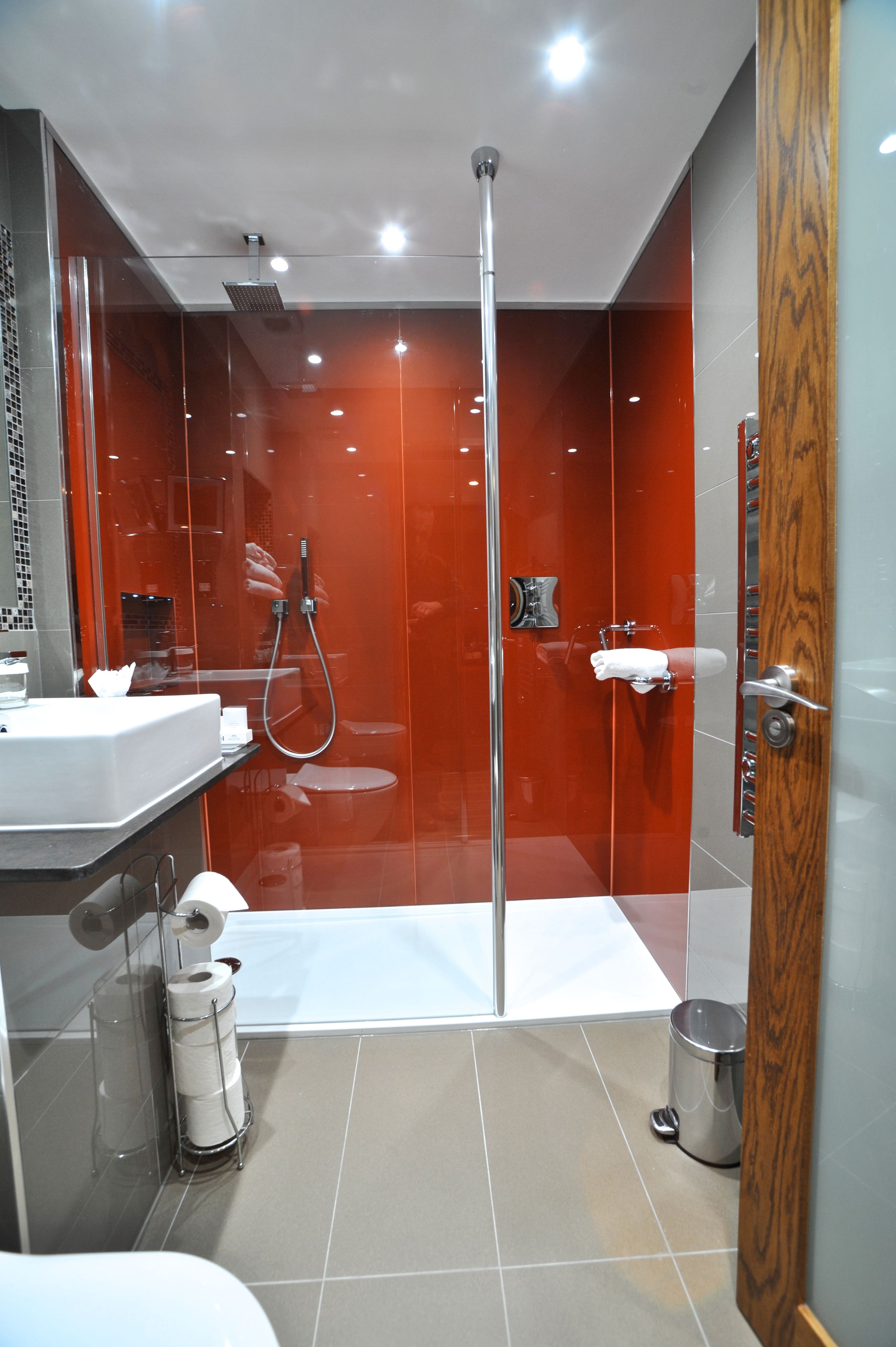 A modern bathroom with a glass-enclosed shower, a white sink, and a wooden door.
