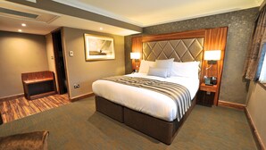 A hotel room with a large bed, two bedside tables with lamps, a wooden bench, and a framed picture on the wall. - Frensham Pond Country House Hotel & Spa (Farnham)