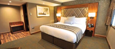A hotel room with a large bed, two bedside tables with lamps, a wooden bench, and a framed picture on the wall.