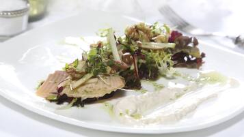 A white plate with a seafood dish, possibly salmon, accompanied by greens and a creamy sauce.
