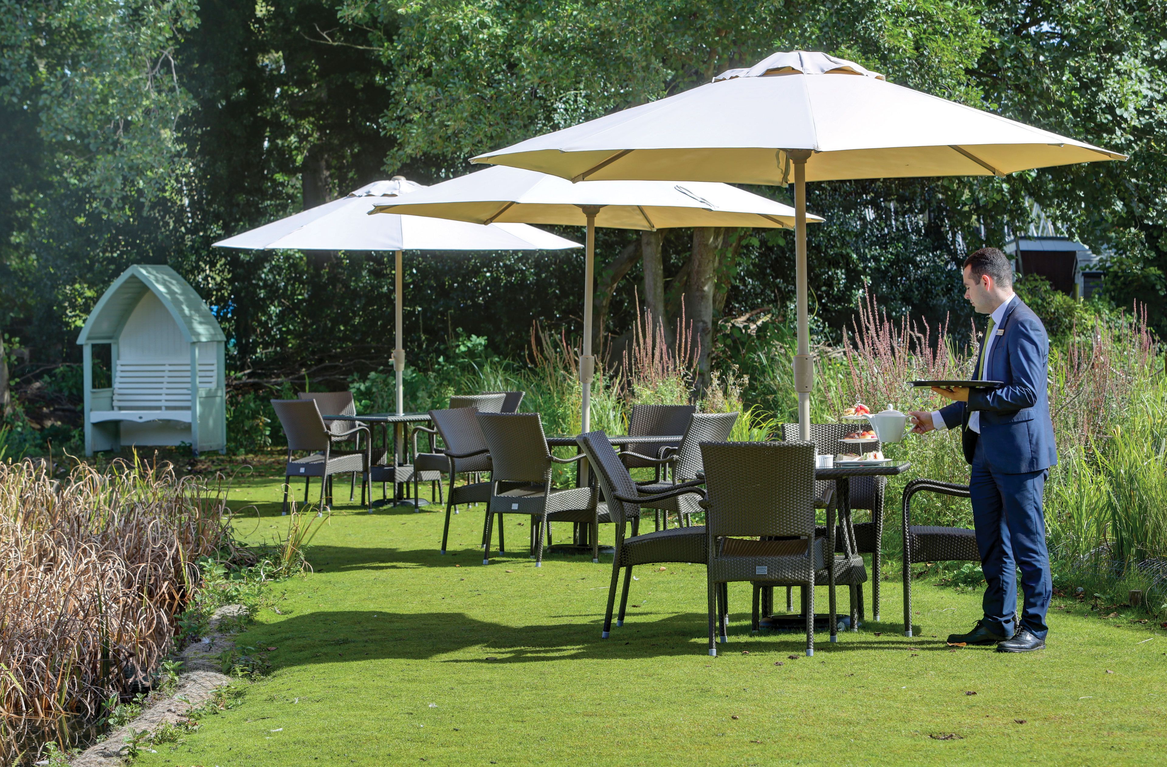 An outdoor seating area with tables and chairs under umbrellas, surrounded by greenery.