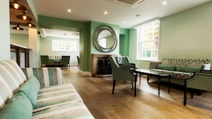 A spacious living area with a fireplace, striped sofa, and green armchairs. - Frensham Pond Country House Hotel & Spa (Farnham)