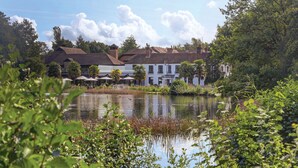 A lakeside hotel with a thatched roof, surrounded by lush greenery and a calm lake. - Frensham Pond Country House Hotel & Spa (Farnham)