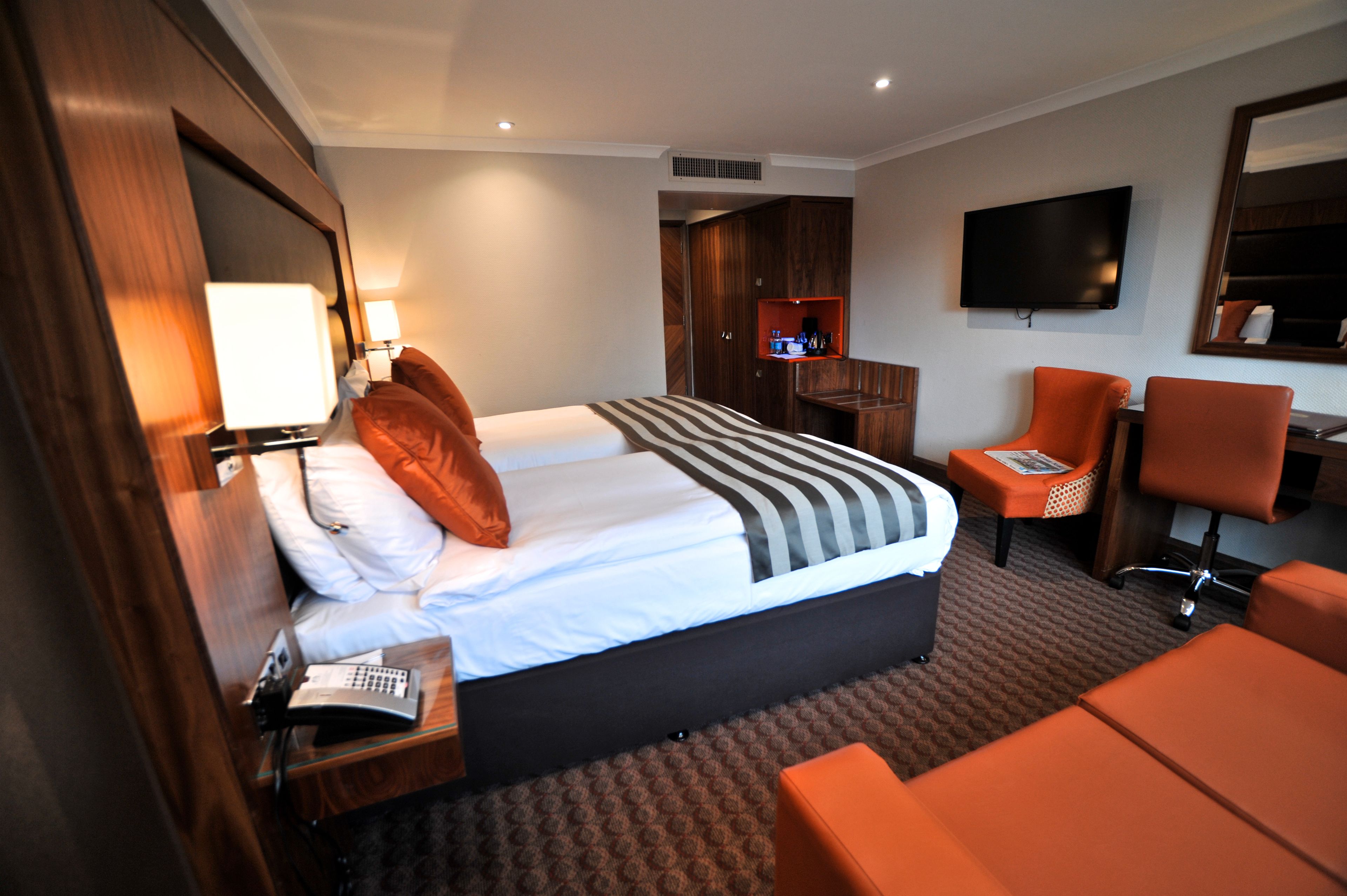 A hotel room with a large bed, a desk, a chair, a TV, and a mirror.