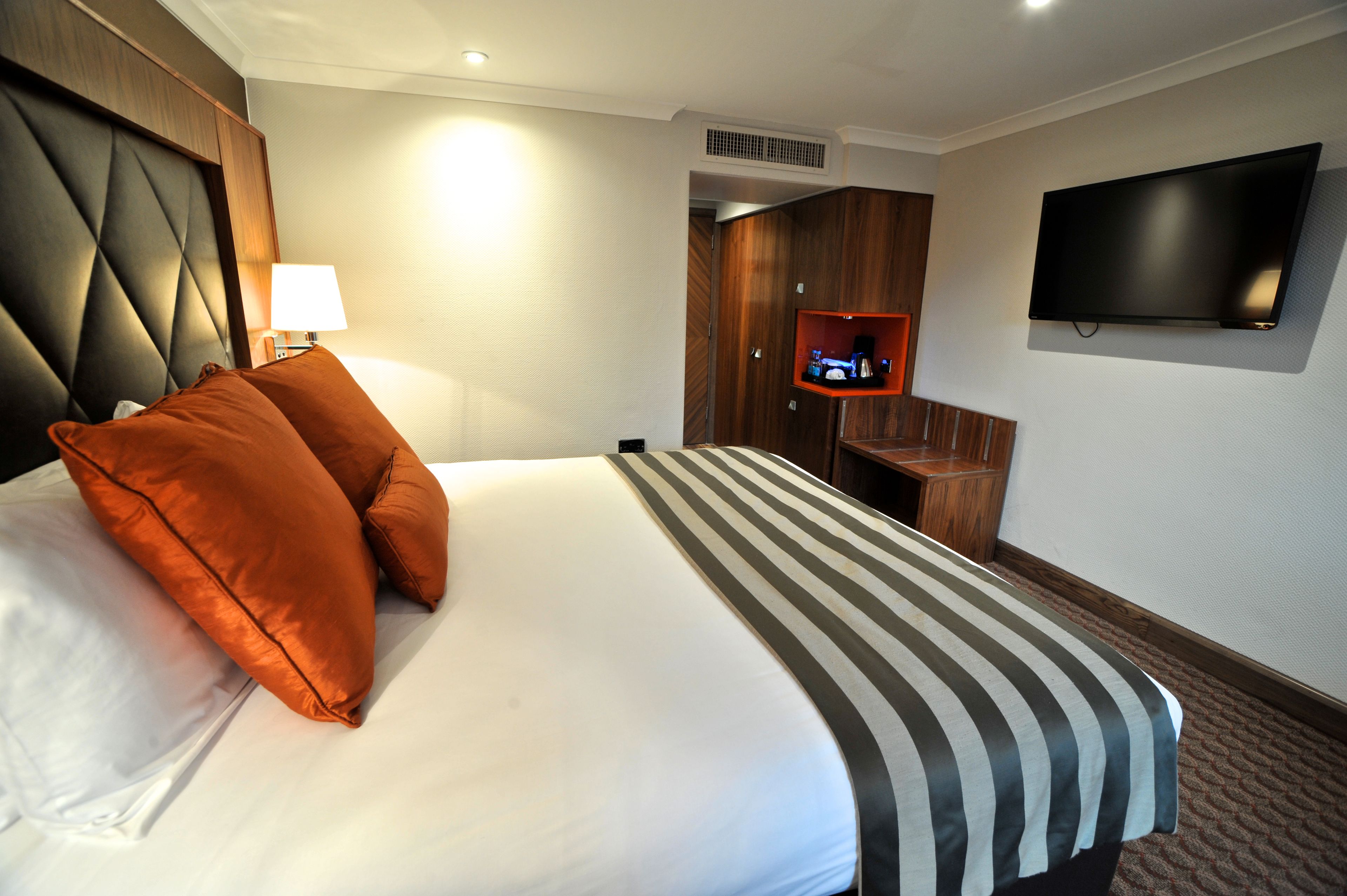 A hotel room with a large bed, a TV mounted on the wall, and a wooden wardrobe.
