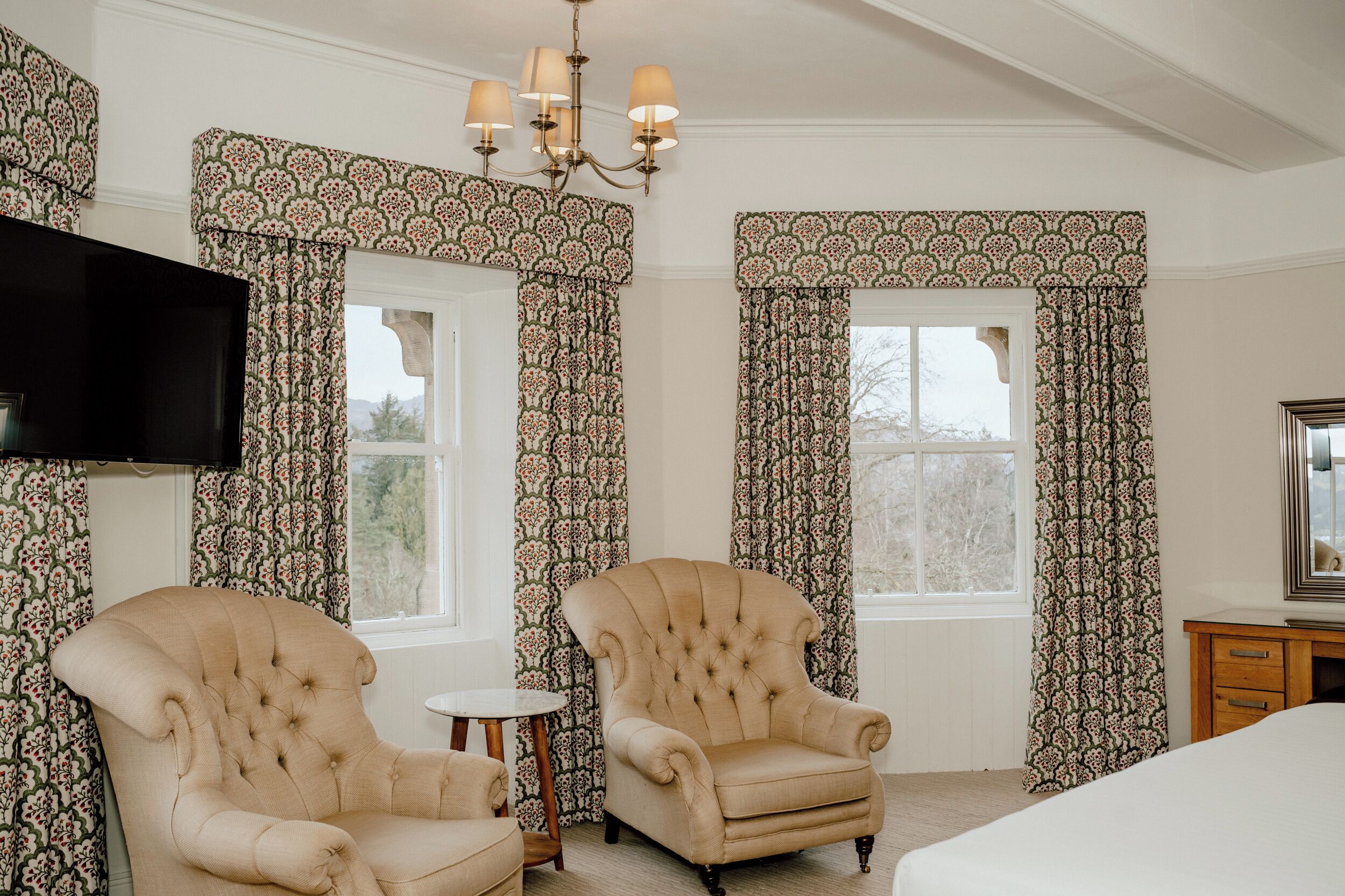 A bedroom with two armchairs, a TV, a small round table, and a bed.