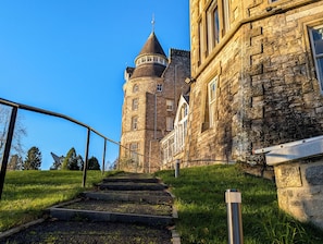 A stone building with a tower, a staircase leading up to it, and a clear blue sky. - Atholl Palace Hotel (Pitlochry)