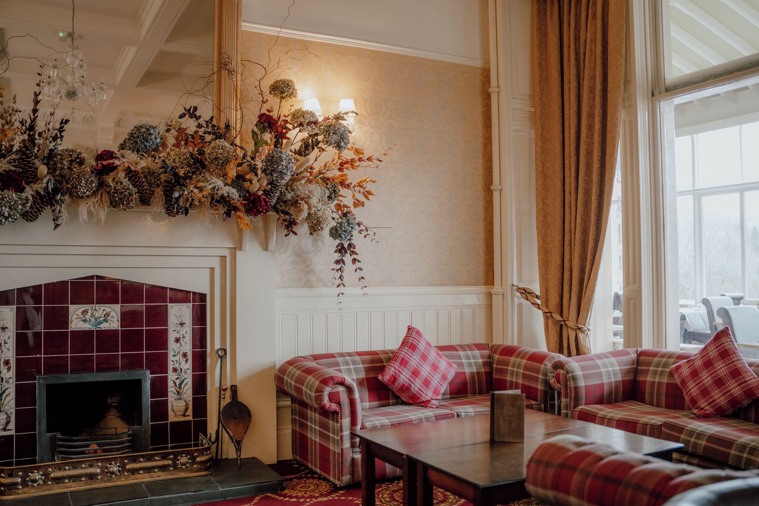 A cozy living room with a fireplace, a sofa set, and a large floral arrangement.